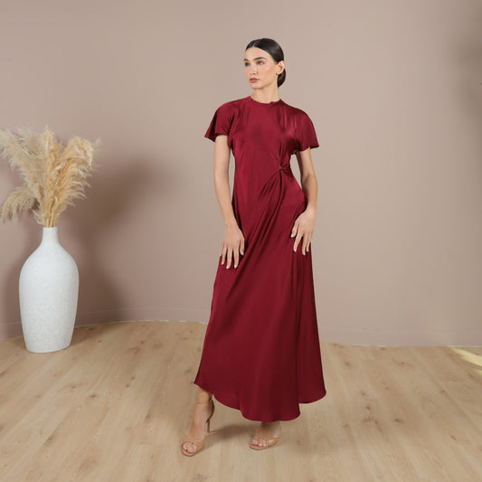 A woman standing in a maroon dress with short sleeves and a round neckline, made from a lightweight fabric.