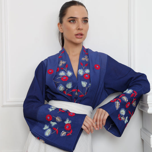 Woman wearing a blue embroidered jacket against a white wall