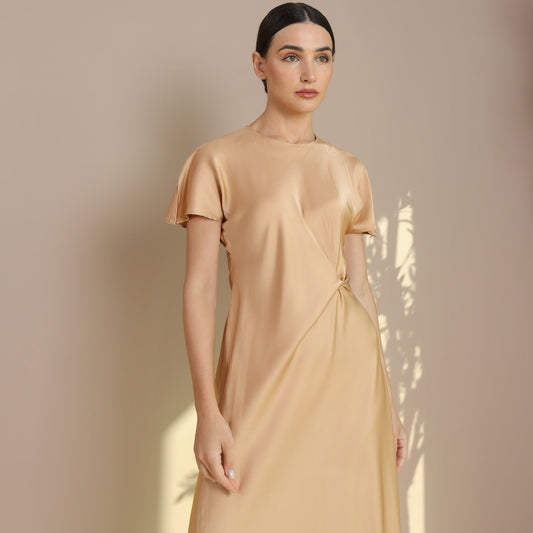 A woman wearing a gold-colored, short-sleeved, maxi dress with a V-neckline, made from silk fabric.